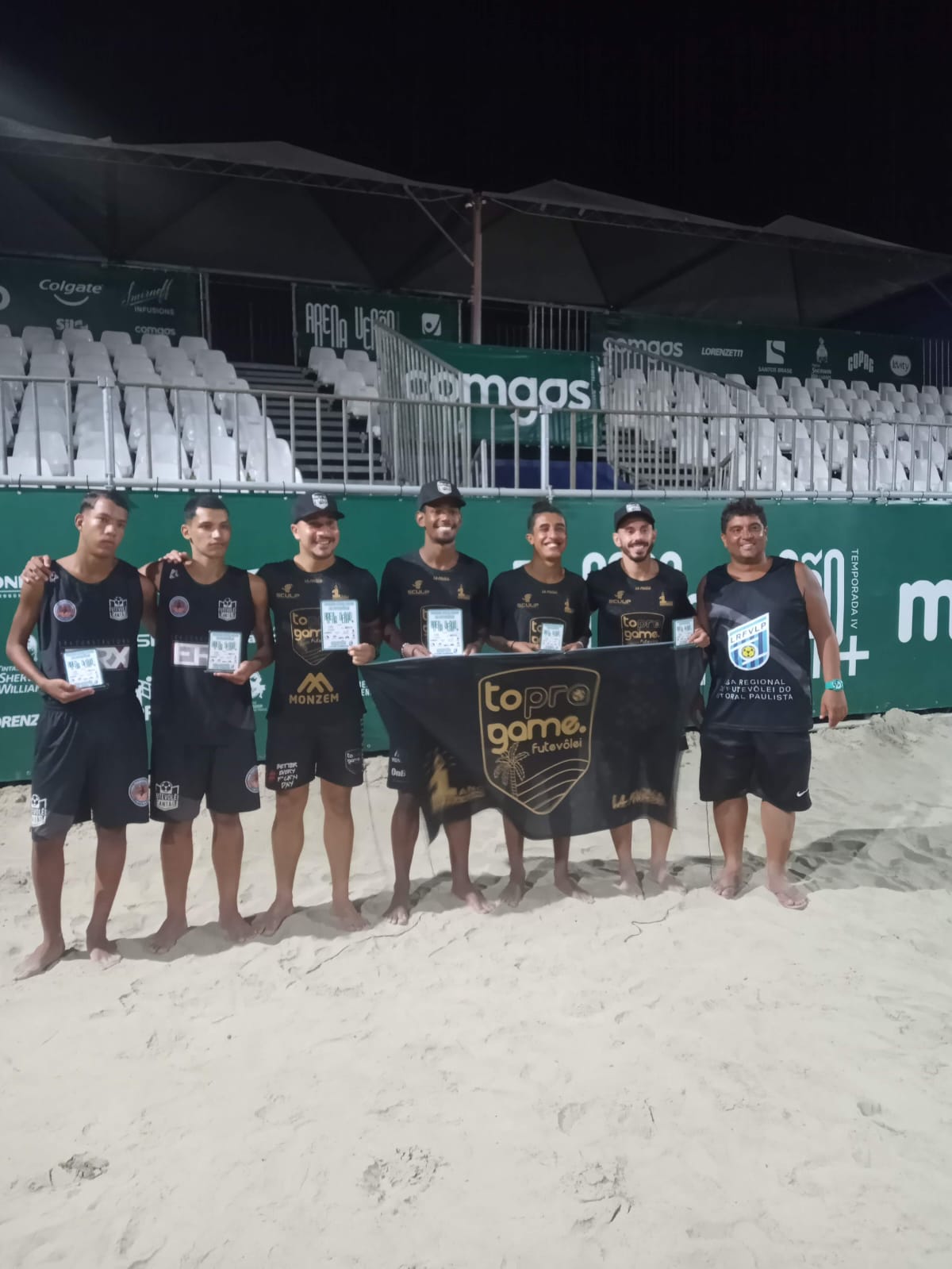 Membros da LRFVLP e atletas campeões segurando troféus e a bandeira do evento 'To Pro Game'